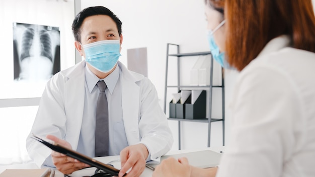 Médico sério da Ásia usando máscara protetora usando tablet está dando uma ótima palestra, discute os resultados