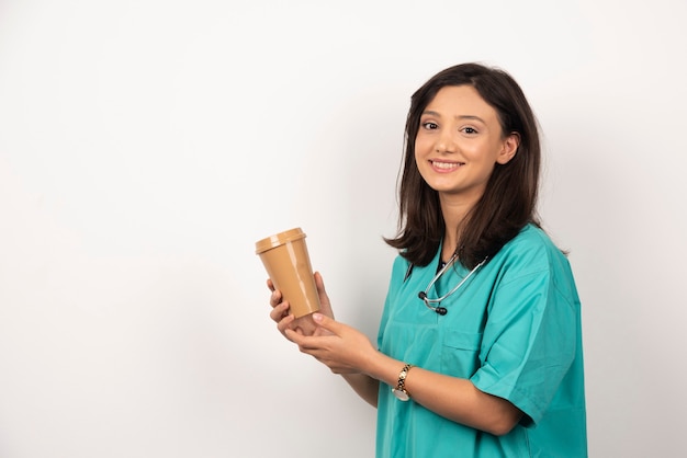 Médico sorridente com estetoscópio segurando o copo no fundo branco. Foto de alta qualidade