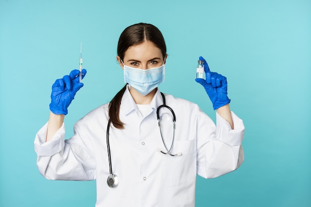 Médico sorridente da equipe médica em máscara facial e luvas de borracha mostrando seringa e vacina de p...