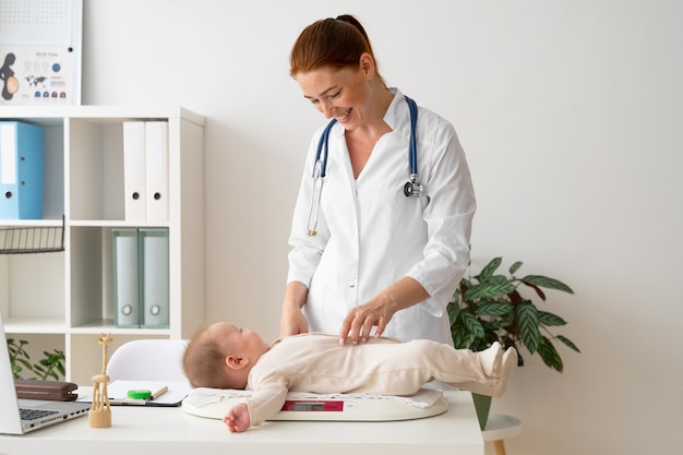 Médico sorridente de tiro médio olhando para o bebê