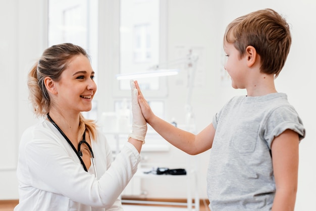 Médico tiro médio e criança levantando a mão