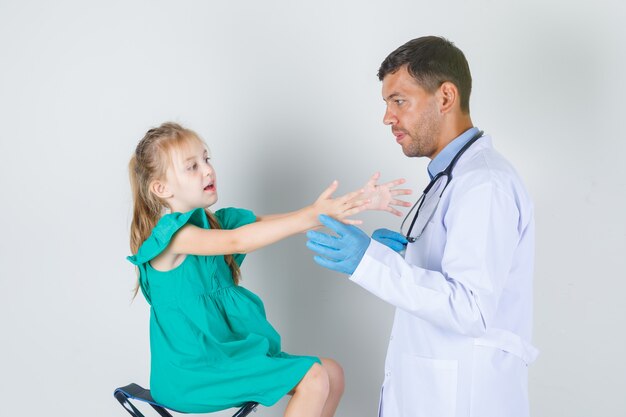 Médico tocando o braço esticado da menina em uniforme branco, luvas