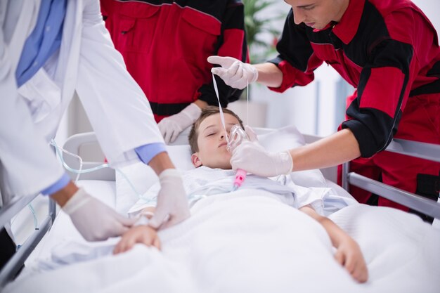 Médicos ajustando máscara de oxigênio enquanto apressam o paciente na sala de emergência