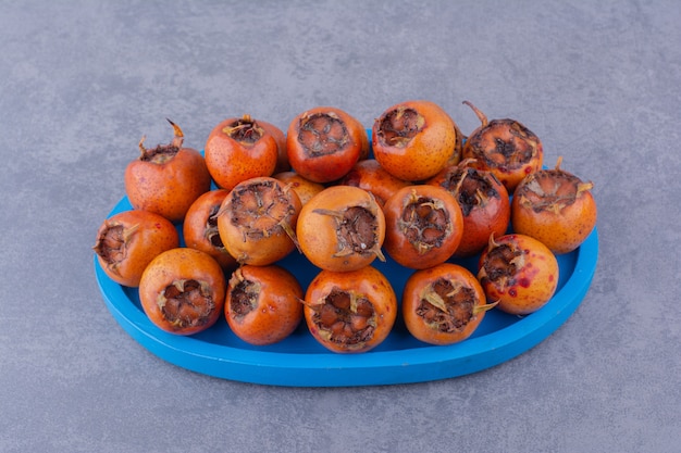 Foto grátis medlars em uma bandeja azul sobre fundo cinza.