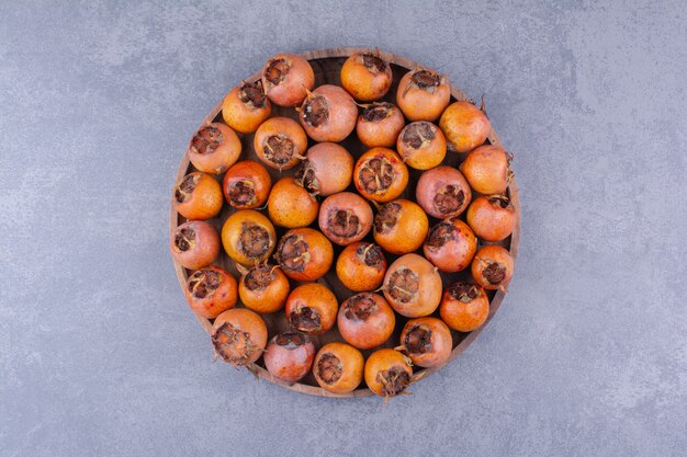 Medlars em uma bandeja de madeira em fundo cinza.