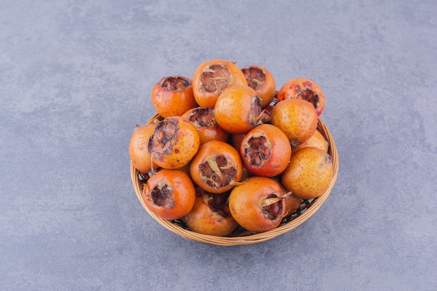 Medlars em uma bandeja de madeira em fundo cinza.