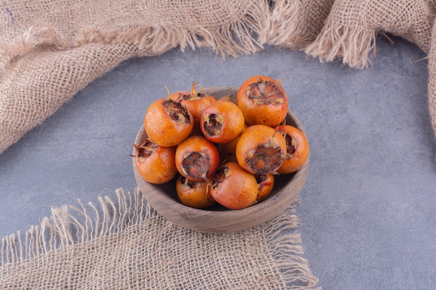 Medlars em uma bandeja de madeira em fundo cinza.