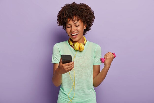 Meia cena de uma feliz instrutora de fitness feminina de pele escura checando a música na playlist