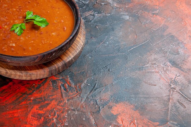 Meia dose de sopa de tomate em uma tábua de corte marrom em uma mesa de cores variadas