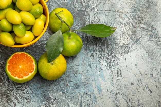 Meia dose de um balde amarelo cheio de tangerinas verdes frescas e tangerinas cortadas pela metade em fundo cinza