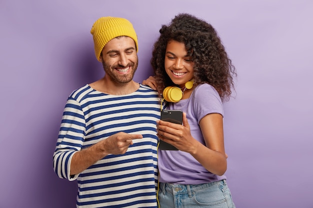 Foto grátis meia foto de namorada e namorado felizes assistindo conteúdo de vídeo engraçado no smartphone, fique perto, tenha expressões alegres, conectado à internet sem fio