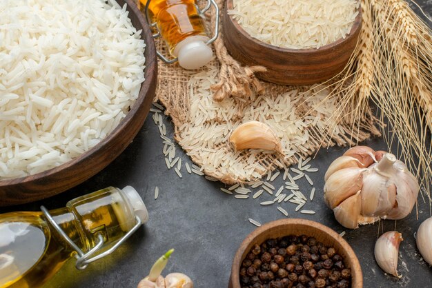 Meia foto de tigelas marrons de arroz longo perfeitas em garrafas de óleo caídas de toalha de cor nua alhos pimentas em fundo escuro