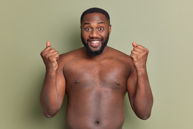 Meia foto de um homem negro alegre celebrando o sucesso fecha os punhos e sorri amplamente