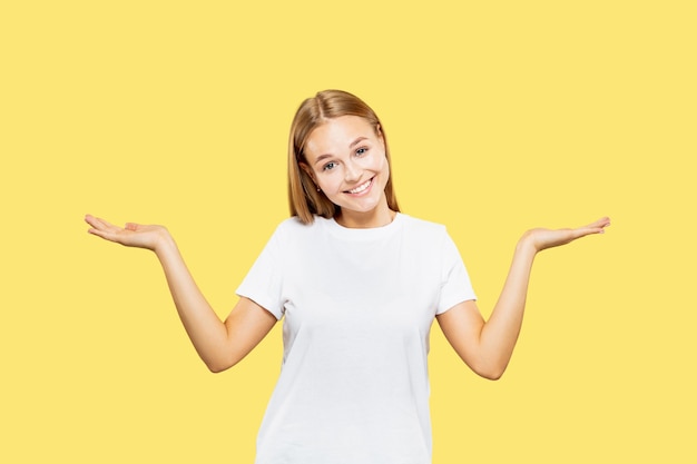 Meio comprimento do retrato de mulher jovem caucasiana em fundo amarelo do estúdio. Linda modelo feminina em camisa branca