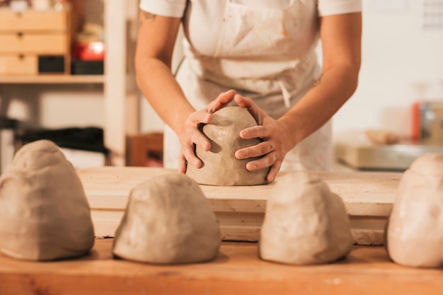 Meio de artesã feminina dando forma ao barro na mesa de madeira