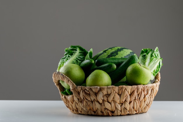 Melancia com alface, maçã, pepino em uma cesta de vime na mesa branca e cinza