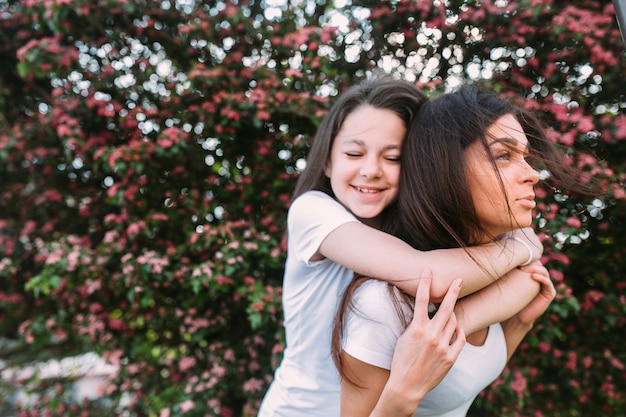 Menina, abraçando, mulher, posar, contra, florescendo, árvore