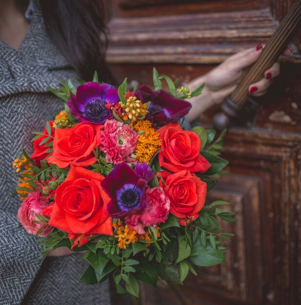 Menina abrindo a porta com um buquê de flores vermelhas e violetas.