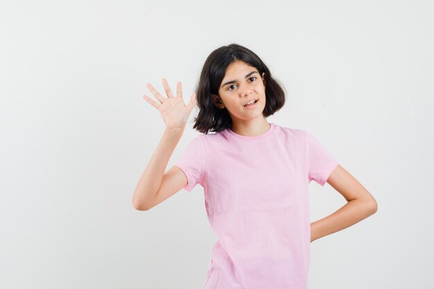 Menina acenando com a mão para dizer adeus na vista frontal da t-shirt rosa.