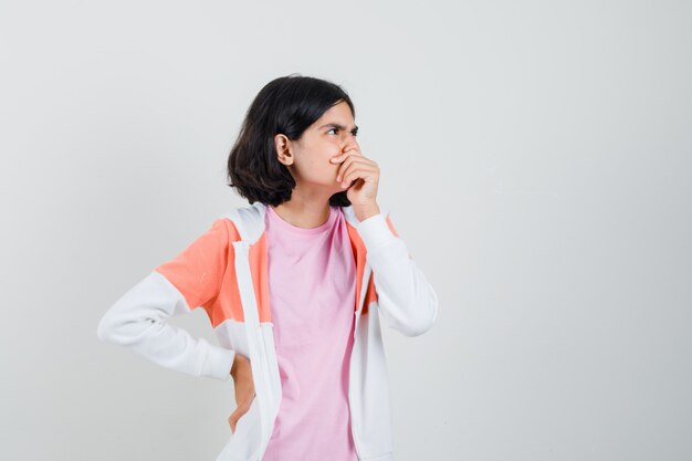 Menina adolescente analisando algo na jaqueta, camisa rosa e parecendo pensativa.