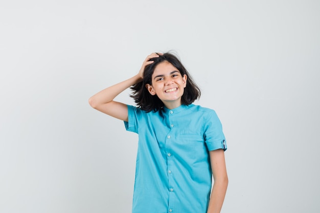 Menina adolescente com camisa azul segurando a mão na cabeça enquanto posa e parecendo otimista