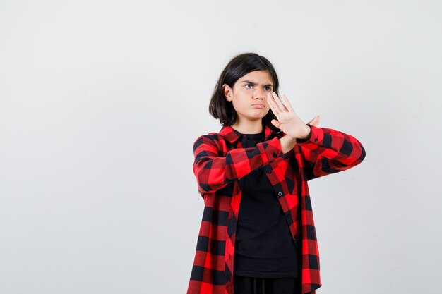 Menina adolescente em camisa casual, mostrando o gesto de golpe de caratê e olhando confiante, vista frontal.