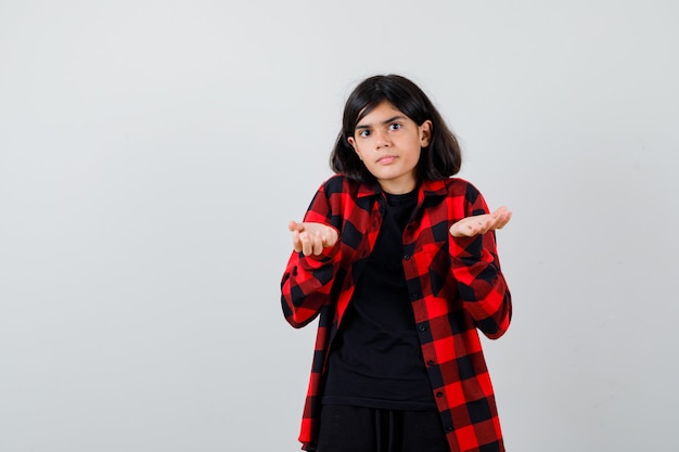 Menina adolescente em camisa casual, mostrando um gesto desamparado e olhando perplexa, vista frontal.