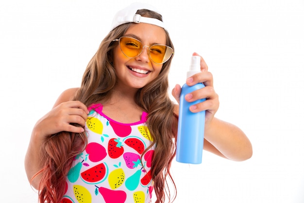 Menina adolescente em copos com creme para bronzear-se em um frasco de spray na parede branca