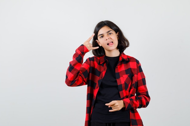 Menina adolescente em t-shirt, camisa quadriculada, mostrando o gesto de rocha e parecendo autoconfiante, vista frontal.