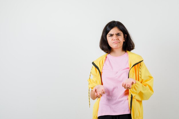 Menina adolescente em um agasalho amarelo, t-shirt, ficando descontente com a pergunta idiota e parecendo triste, vista frontal.