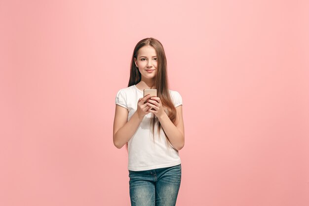 Menina adolescente feliz em pé, sorrindo com o celular em um estúdio rosa moderno
