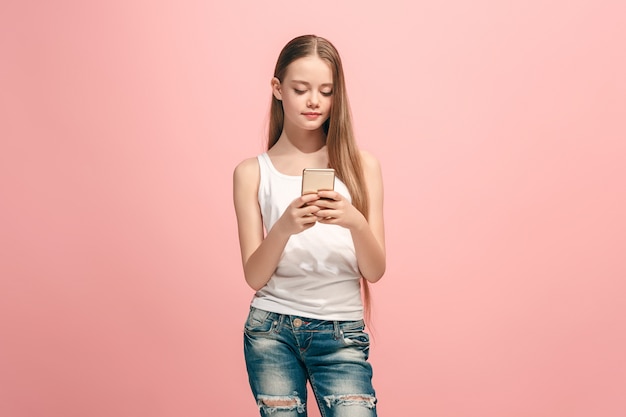 Menina adolescente feliz em pé, sorrindo com o celular em um estúdio rosa moderno