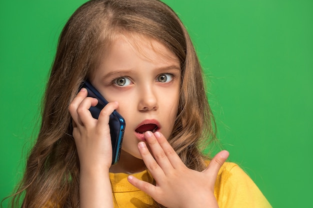 Menina adolescente feliz em pé, sorrindo com o celular, na parede verde da moda. belo retrato feminino de meio corpo. emoções humanas, conceito de expressão facial.