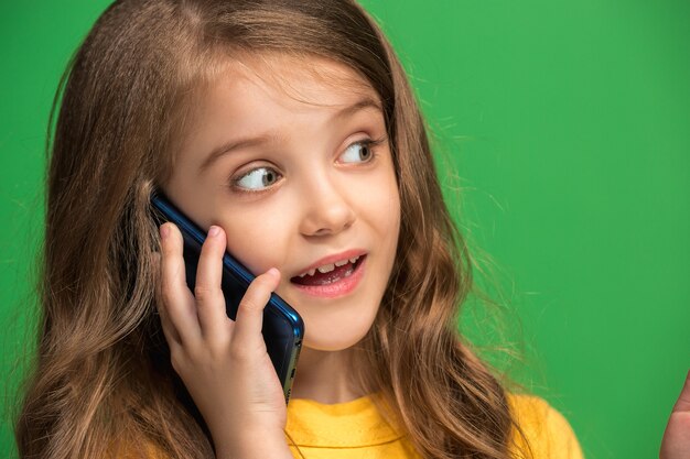 Menina adolescente feliz em pé, sorrindo com o celular sobre o fundo do estúdio verde da moda