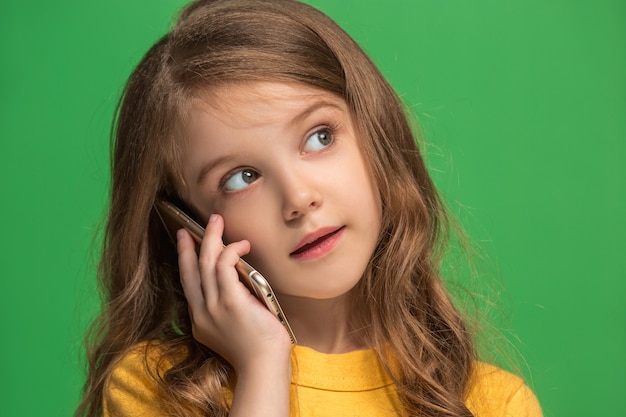 Menina adolescente feliz em pé, sorrindo com o celular sobre o fundo do estúdio verde da moda