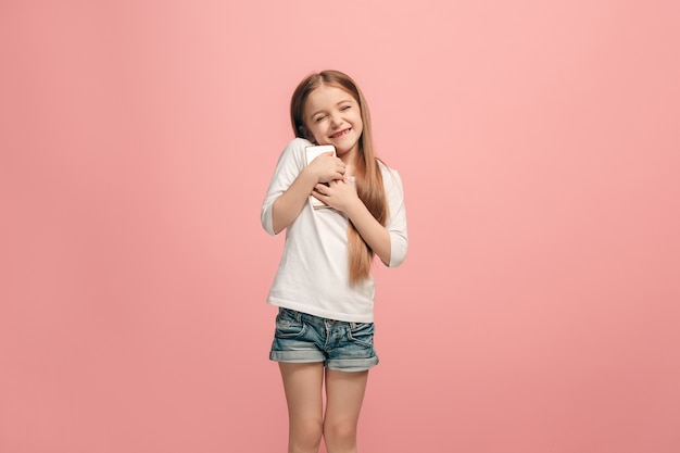 Foto grátis menina adolescente feliz em pé, sorrindo com o celular sobre o fundo rosa da moda do estúdio.