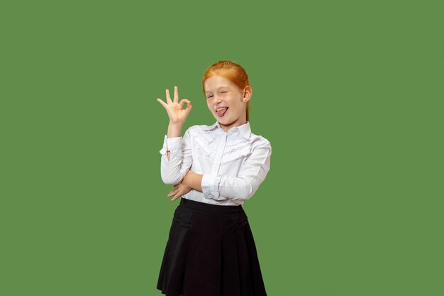 Menina adolescente feliz em pé, sorrindo e apontando para si mesmo, isolado no fundo do estúdio verde na moda. Belo retrato feminino de meio corpo. Emoções humanas, conceito de expressão facial.