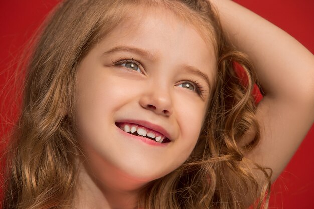 Menina adolescente feliz em pé, sorrindo isolada em vermelho na moda. Belo retrato feminino.