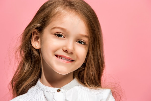 Menina adolescente feliz em pé, sorrindo isolado na parede rosa da moda. Belo retrato feminino. Jovem satisfazer a garota. Emoções humanas, conceito de expressão facial. Vista frontal.