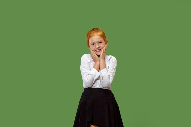 Menina adolescente feliz em pé, sorrindo isolado no fundo do estúdio verde da moda.