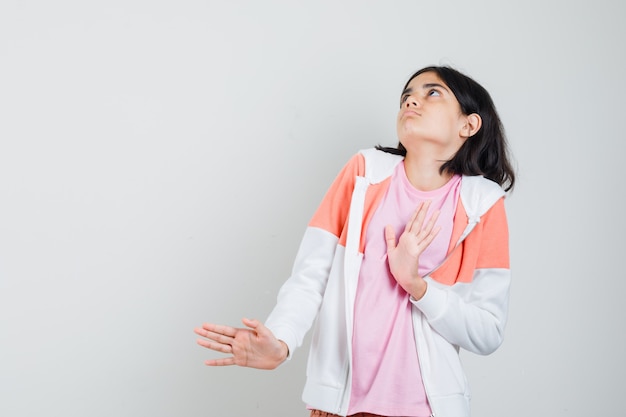 Menina adolescente levantando as mãos para rejeitar algo na jaqueta, camisa rosa e parecendo relutante.