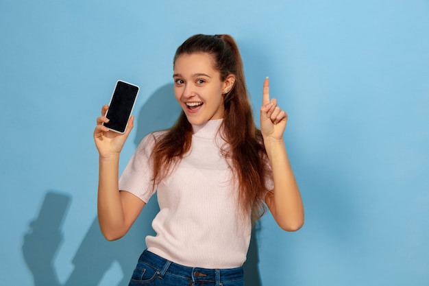 Menina adolescente mostrando a tela do telefone, apontando para cima