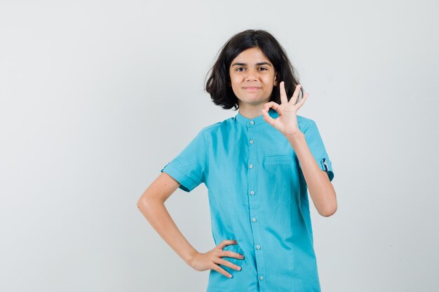 Menina adolescente mostrando o gesto ok na camisa azul e parece feliz.