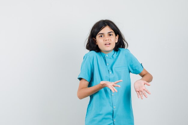 Menina adolescente mostrando um gesto desamparado na camisa azul e parecendo descontente.