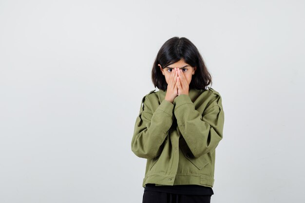 Menina adolescente segurando as mãos na boca em uma camiseta, jaqueta e parecendo assustada. vista frontal.