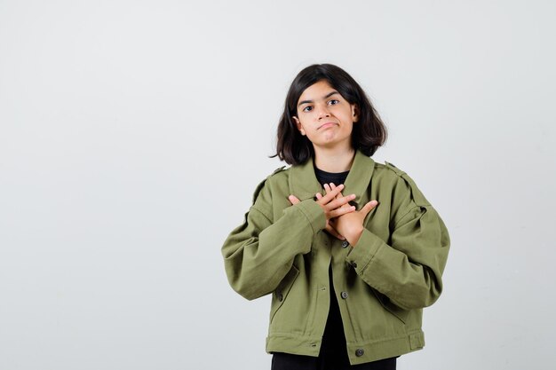 Menina adolescente segurando as mãos no peito em t-shirt, jaqueta e parecendo imprudente. vista frontal.