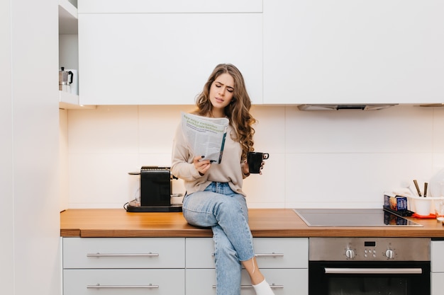 Menina adorável concentrada lendo revista enquanto toma chá