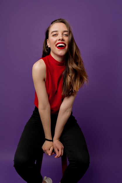 Menina adorável e sensual com um sorriso maravilhoso usando uma blusa vermelha rindo em violeta