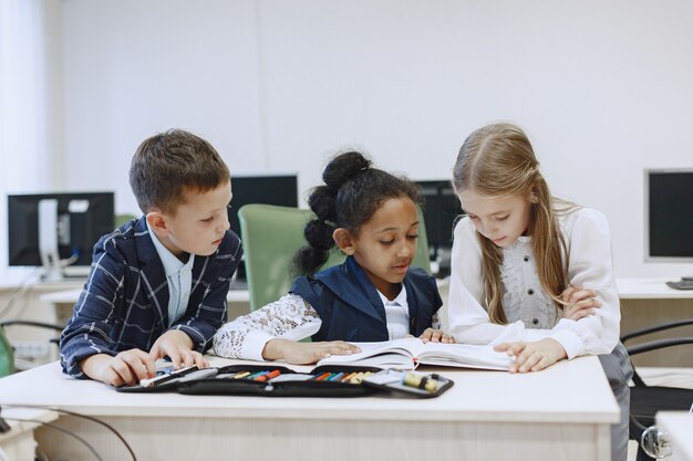 Menina africana sentada à mesa. Colegiais lêem um livro durante um intervalo. Crianças sentam em uma aula de ciência da computação.