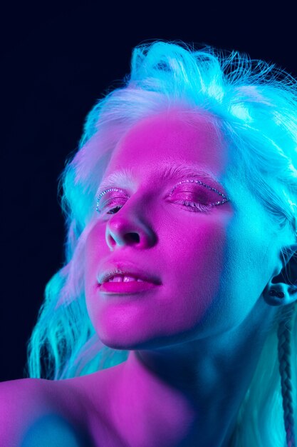 Menina albina com pele branca, lábios naturais e cabelo branco em luz de néon, isolado no fundo preto do estúdio.